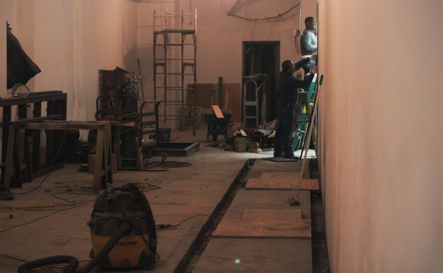 Workers on the main floor close off a former eyeglass store as they prepare to install electrical switching equipment.