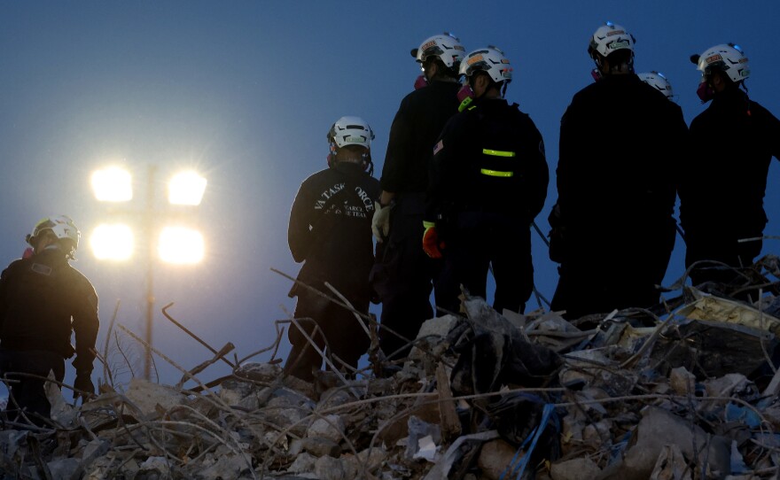 Workers oversee an excavator dig through the rubble of the collapsed 12-story Champlain Towers South condo building on Friday.