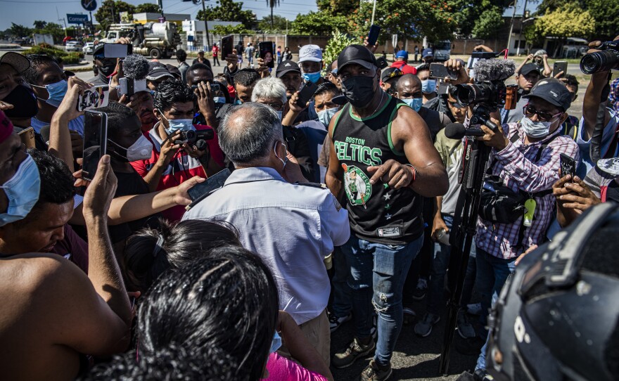 Cuban Heidel Roberto, right, complains to Hugo Salvador Cuéllar of the INM about the lack of buses. The slow deployment of northbound buses has frustrated many Haitians and other migrants who are unhoused in Tapachula.