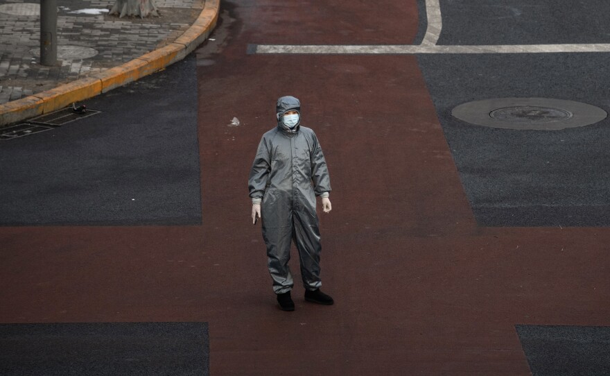 A Chinese woman wears a protective suit and mask as she waits to cross the intersection of a nearly empty Beijing on Saturday.