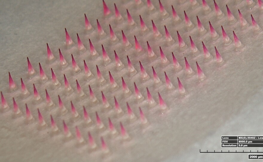 A magnified image shows a patch with its microneedles dyed pink.