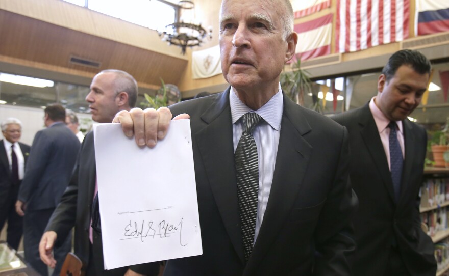 Gov. Jerry Brown holds up a copy of the education bill he signed during a ceremonial signing at California Middle School in Sacramento on July 1, 2013.