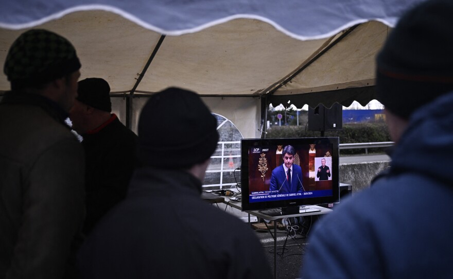 French farmers watch a broadcast of French Prime Minister Gabriel Attal delivering his government's policy statement at the National Assembly, as they take part in a roadblock protest on the A6 highway near Lisses, south of Paris.