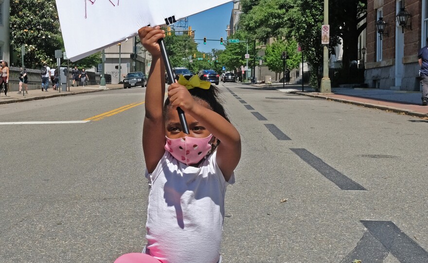 Nasiah Morris, 4, of Richmond, carries a sign during a march from Brown's Island to the 17th Street Market in Shockoe Bottom, June 7. The youngster, kneeling at 9th and Grace streets across from the State Capitol, attended the rally with her mother, Toya Morris, and 15-year-old brother, Tye.