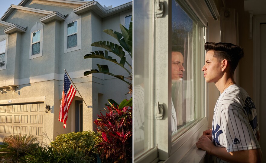 A U.S. flag hangs on the wall of a house in Tampa, Florida. Yossell Machado Fígueredo, 21, looks out the window of his room. Like most Cubans in recent years, Yossell arrived at the southern border through a journey with his mother and sister by land from Nicaragua.