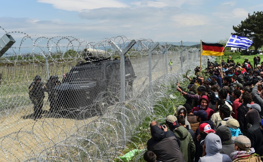 Refugees and migrants bearing Greek and German flags face Macedonian soldiers at the border fence as they protest on Monday, a day after violence broke out at the border.