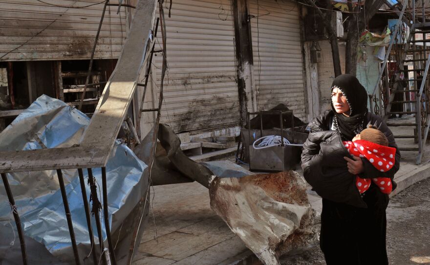A Syrian woman carries an infant Thursday past the ruins of a restaurant in Manbij that was targeted by the Islamic State. Four Americans were killed in the attack.