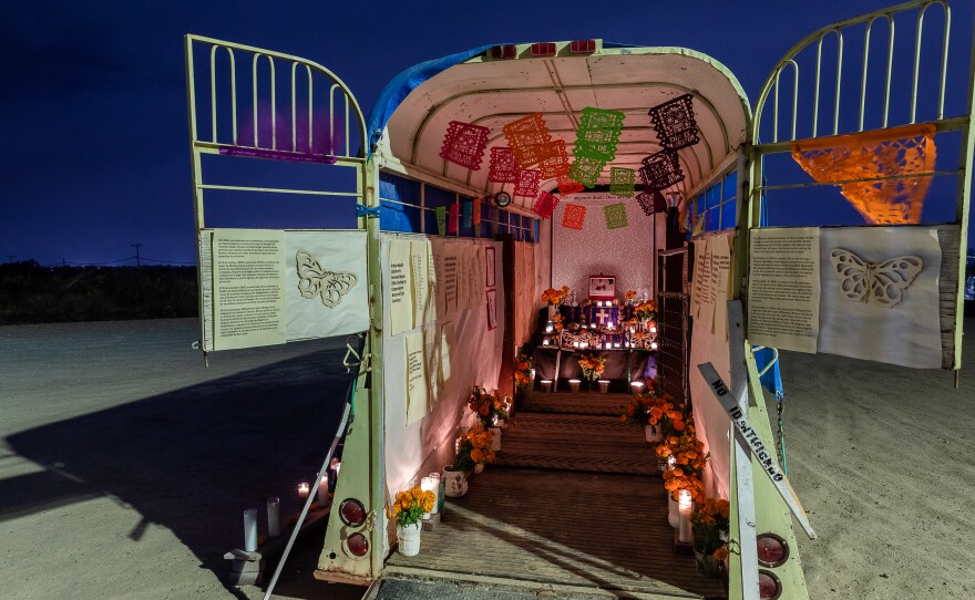 Dozens of candles illuminate the Dia de los Muertos ofrenda honoring migrants who died crossing the border illegally.