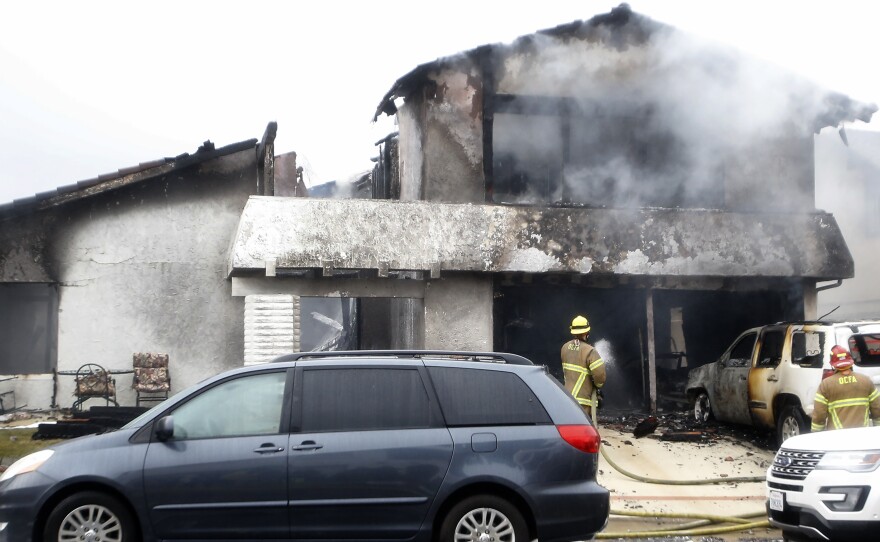 Firefighters work in the driveway of a house damaged in a deadly plane crash Sunday in Yorba Linda, Calif. Officials say at least five people died, including the pilot and four people who were in the house.