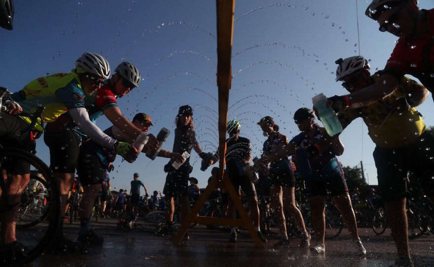 Riders fill up their water bottles at a sprinkler station set up along RAGBRAI's route Wednesday, July 28, in Whittemore, Iowa.