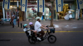 Israeli flags hang at a shop as a bicyclist carrying children passes by, Wednesday, Oct. 28, 2026, in Tel Aviv, Israel, the day after Israel's general election.