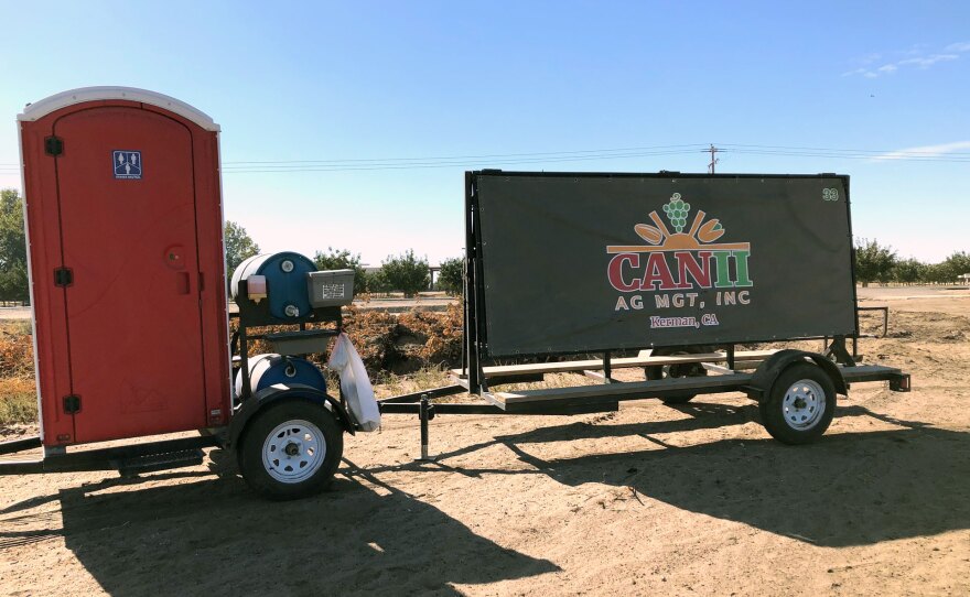 A banner for Can II Ag Mgt. stands next to a portable toilet at a field in Fresno County where farmworkers said the company failed to offer them N95 masks or other required protections during heavy smoke days.