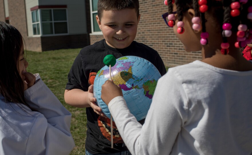 Second graders Hanah Sung, Izaac Stuck and Amaurie Robinson simulate an eclipse by casting a shadow with a play dough moon on an inflatable globe. Their teacher, Natasha Cummings, directs them to aim the shadow over the spot on the globe where Indianapolis would be.