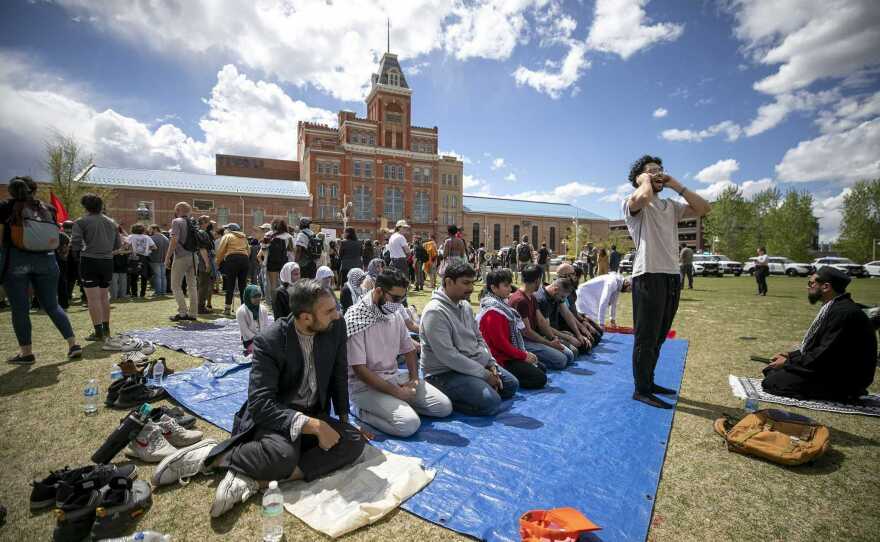 Men pray while police arrest protesters nearby.