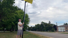 Brady O'Rourke in Crystal, Minn., holds a sign he made to block the view of a Flock camera, which tracks vehicles driving along the road. It's one of several actions Americans are taking to oppose this police surveillance technology.