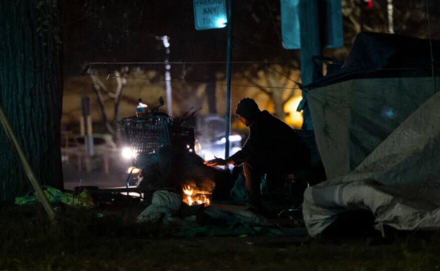 Muhammad, who declined to provide his last name, warms his hand at a fire near his tent in Sacramento on Feb. 24, 2022.