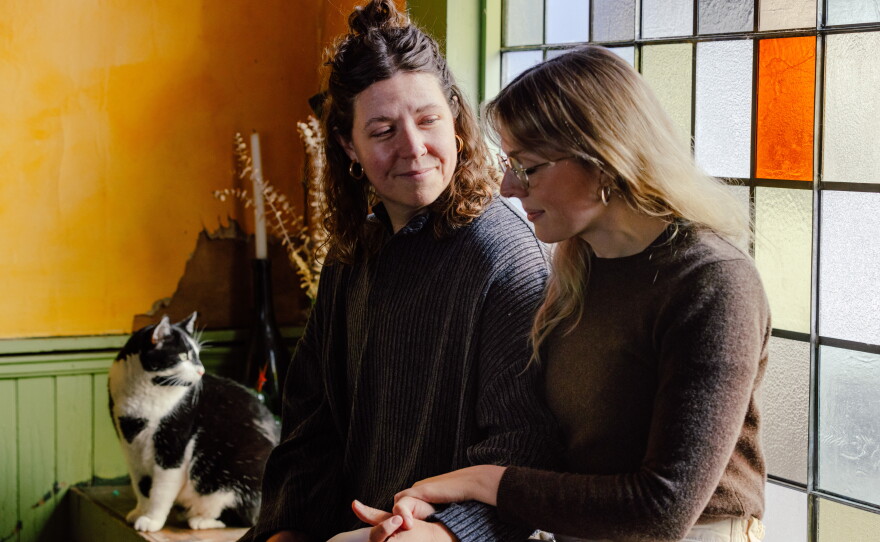 Emma Brennan, Lauren Wright and their cat, TV, sit in their home, in Baltimore, Md., on Tuesday.