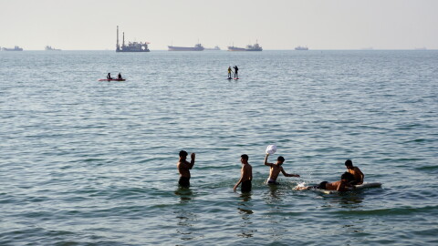Residents swim and play in the waters of the Strait of Hormuz while cargo ships and commercial vessels lie anchored in the distance off Bandar Abbas, Iran, Wednesday, June 10, 2026.