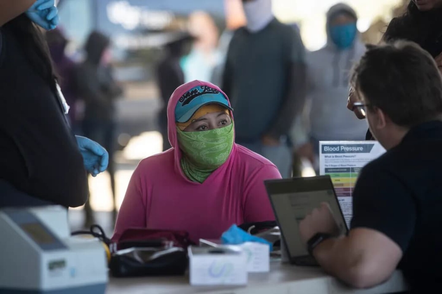 Farmworkers line up in an equipment barn to get a check-up by the staff of UCSF-Fresno, part of the Rural Mobile Health program, at a farm outside of Helm on June 16, 2025.
