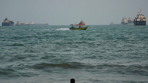 A swimmer remains near the shore as a motorboat passes commercial vessels anchored in the Strait of Hormuz off Bandar Abbas, Iran, on Friday.