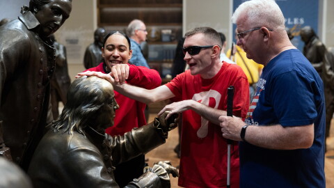 The National Constitution Center in Philadelphia offers guided tactile tours aimed at blind and low vision visitors in a gallery called Signers' Hall. Museum educator Sydney Wharton traces visitor Tim Kelly's Jr. hands over the statue of Benjamin Franklin as she leads him and his father, Tim Kelly Sr., through the gallery.
