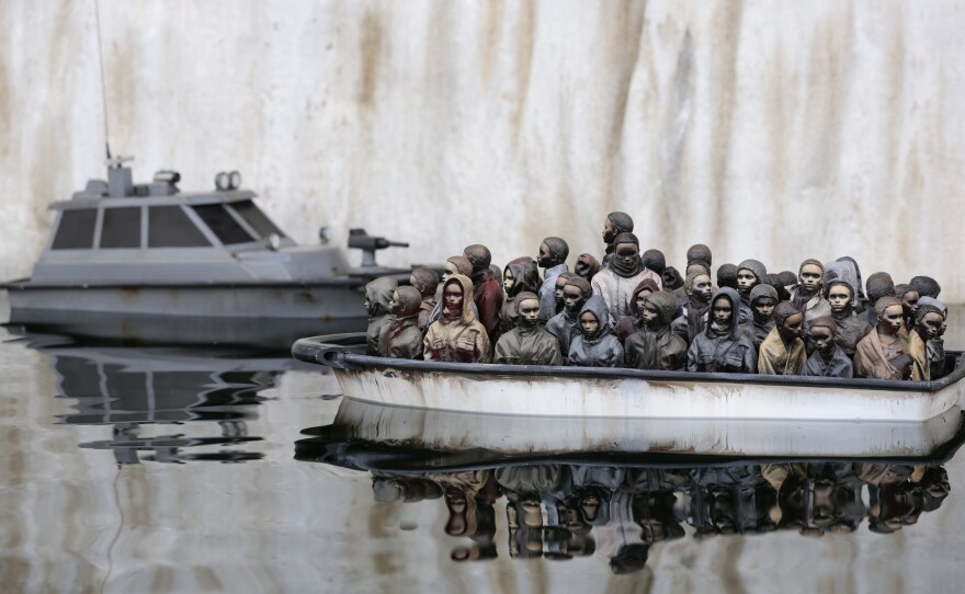 This art exhibit shows a boat packed with migrants floating in a pond at Banksy's "bemusement park" called Dismaland. Now, the park is being dismantled and the materials are being sent to a refugee camp in France to be used for building shelters.