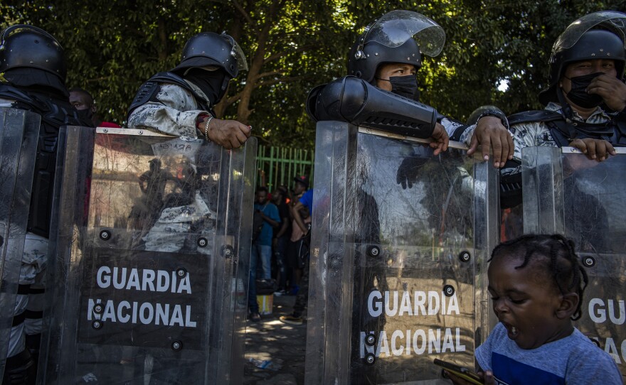 Mexican National Guard troops control the line of migrants waiting for buses in a Tapachula city park.