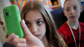 Promotional photo of a girl holding a cell phone at a camp for middle school students offered by the Smithsonian’s Hirshhorn Museum. Kids use mobile devices, augmented reality scenarios, and digital scavenger hunts to explore the content of various museums on the Mall. 