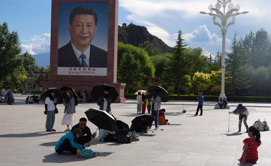 Tourists rest near a portrait of Chinese President Xi Jinping at a public square at the base of the Potala Palace in western China's Tibet autonomous region on July 21, 2026, during a government-organized visit for foreign journalists.