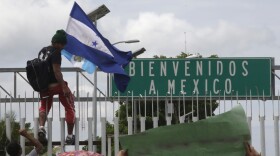 A Honduran migrant hold his national flag, climbs the border fence in Ciudad Hidalgo, Mexico, Friday, Oct. 19, 2018.