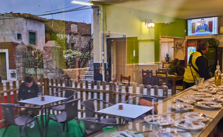 People seen through a window inside a bar in La Cabrera, on the outskirts of Madrid, Spain, watch a televised speech by Spanish Prime Minister Pedro Sanchez from La Moncloa Palace announcing national elections, Monday, Oct. 5, 2026.