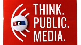 An NPR pin laying on top of a Think Public Media sign.