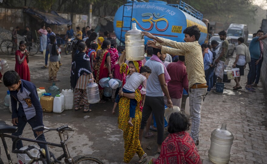 A woman balances a water can on her head while people collect water from a mobile water tanker on World Water Day in a residential area in New Delhi, India.