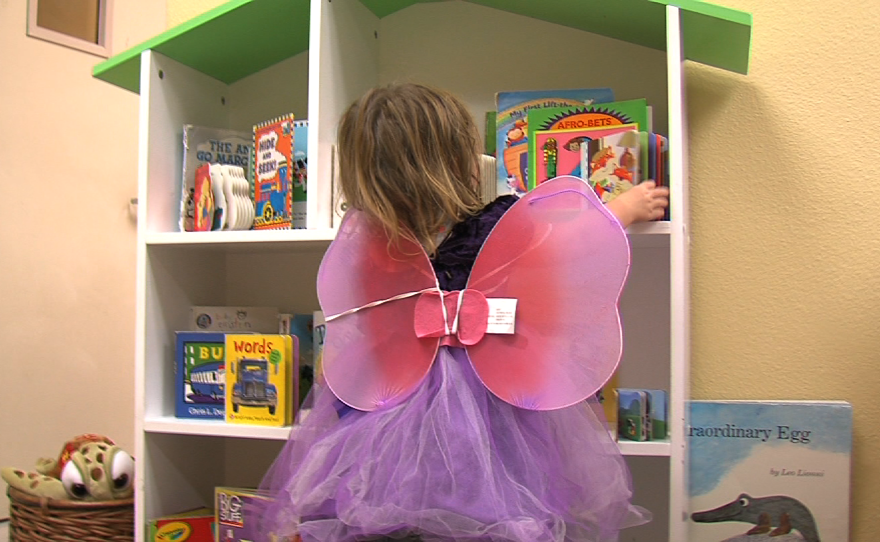 Wearing butterfly wings and a princess dress, 2-year-old Rebeka looks at books at the Rescue Mission's new Children's Center, Sept. 9, 2014.