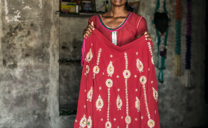Nimmu's older sister, Durga, holds up part of the wedding dress that Nimmu was married in. It was too big for her, Nimmu says, and the embroidery was lame.