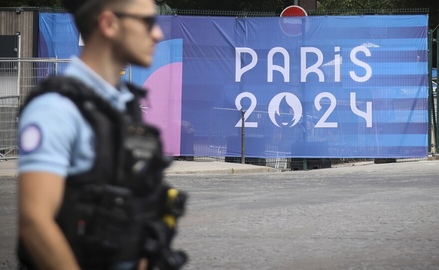 A police officer walks past a Paris Olympics canvas at the 2024 Summer Olympics, Saturday, July 20, 2024, in Paris, France. Three days before the start of the Olympics, France's Interior Minister has hailed the country’s law enforcement for their hard work in making the Paris Games safe for 10,500 athletes and millions of visitors.