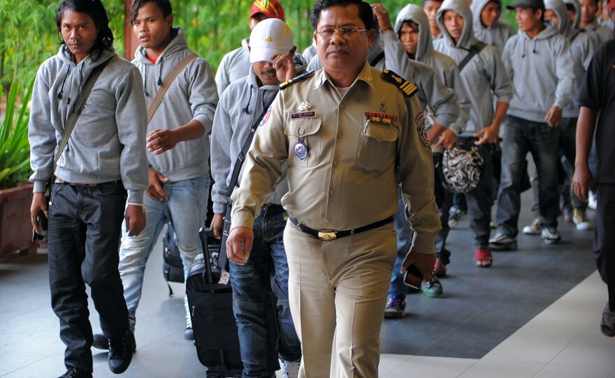 A Cambodian policeman escorts 30 fishermen returning home after being freed or escaping from slave-like conditions on Thai fishing vessels. The men arrived at the Phnom Penh airport in December. Large numbers of men from Myanmar and Cambodia are trafficked onto Thai fishing boats and forced to work in brutal conditions.