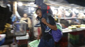 A man carries a child on his shoulders in the rain as a caravan of several hundred migrants set off walking toward the distant U.S. from a main bus station in San Pedro Sula, Honduras, late Monday, Jan. 14, 2019. Yet another caravan of Central American migrants set out Monday from Honduras, seeking to reach the U.S. border, following the same route followed by thousands on at least three caravans last year.