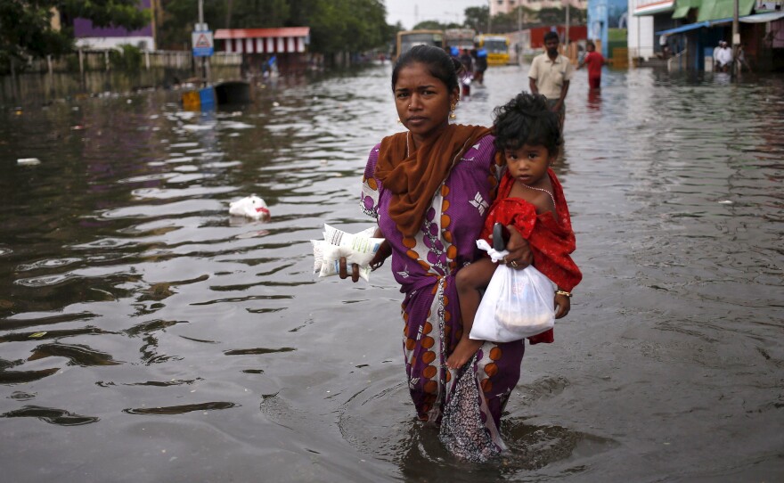 Child and milk packets in hand, a woman wades through a flooded street in Chennai on Saturday.