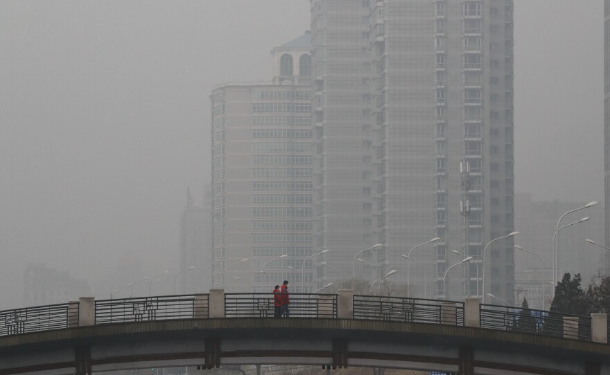 Chinese men wearing masks walk on a bridge near a building shrouded by fog and pollution in Beijing on Jan. 5. China has long faced some of the worst air pollution in the world, blamed on its reliance on coal and older, less efficient cars. Inadequate controls on industry and lax enforcement of standards have worsened the problem.