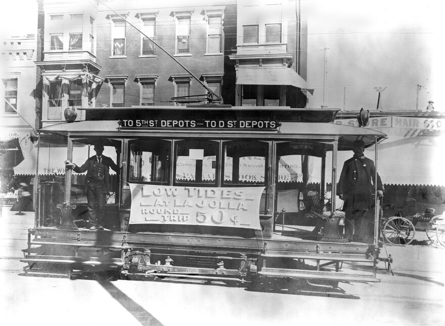 A San Diego Electric Railway streetcar serves the Fifth Street and D Street depots in the late 1890s. A banner advertising "Low Tides at La Jolla" promotes a round-trip beach excursion for 50 cents.
