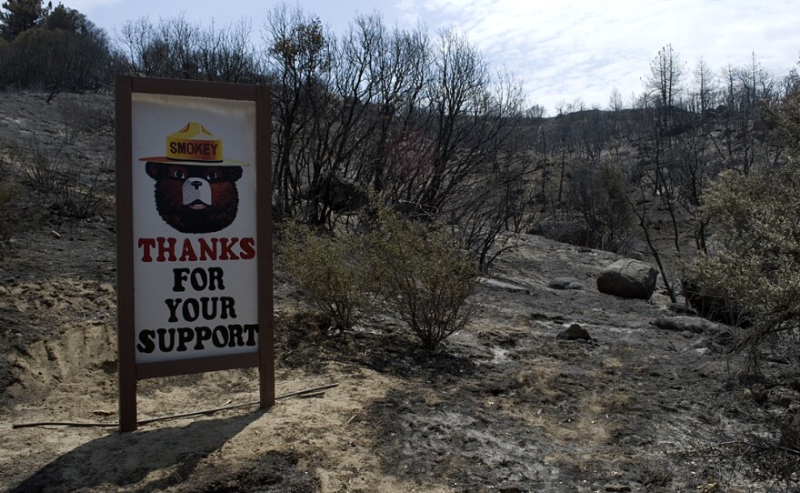 A Smokey the Bear sign stands undamaged by the flames that raced by it two days earlier on their way to engulfing 42 square miles of the San Jacinto Mountains in California. The sign sits next to the Esperanza Firefighters Memorial Highway, named after five firefighters who died battling the Esperanza Fire in similar terrain in 2006.