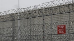 Barbed wire fencing is shown behind a sign in English and Spanish in a recreation yard used by detainees during a media tour of the U.S. Immigration and Customs Enforcement detention center in 2019 in Tacoma, Wash.