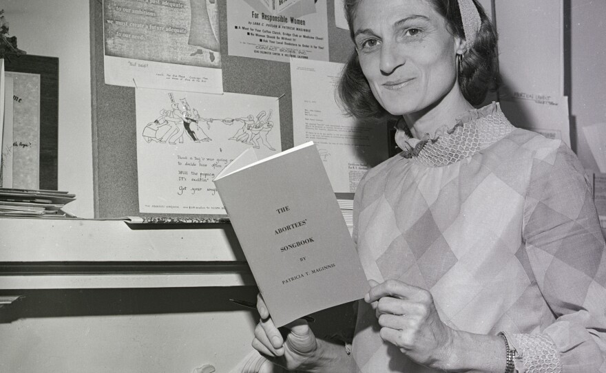 Patricia Maginnis next to a bulletin board full of abortion information and holding her "Abortees' Songbook" in Sausalito, Calif., September 1970.