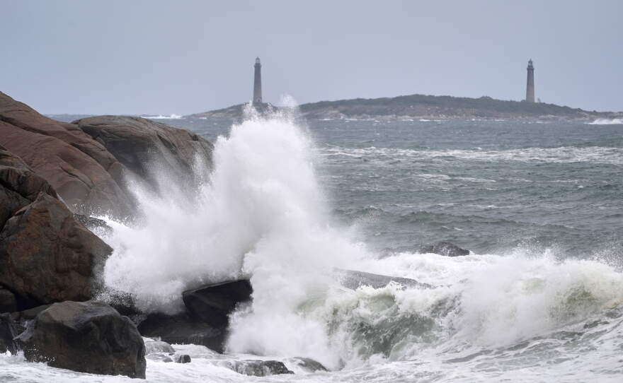Surf breaks along the rocky coastline, with the twin lighthouses of Thatcher Island visible in the distance, during the early stages of a nor'easter Friday, Sept. 25, 2026, in Gloucester, Mass.