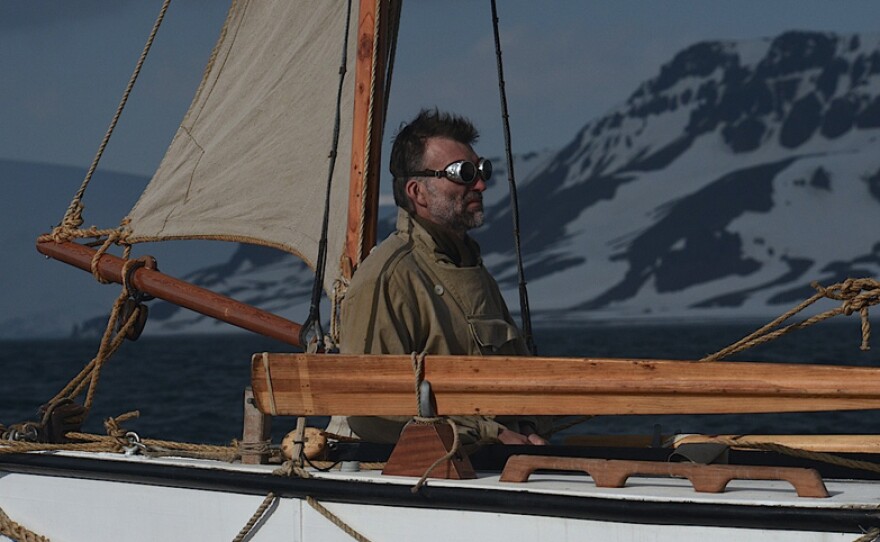 Expedition leader Tim Jarvis at the helm wearing sunglasses.