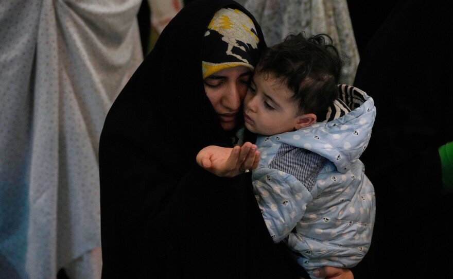 An Iranian worshipper prays during a ceremony to perform Eid al-Fitr prayers marking the end of the holy fasting month of Ramadan while holding a child at the Imam Khomeini Grand Mosque in Tehran, Iran, Saturday, March 21, 2026.