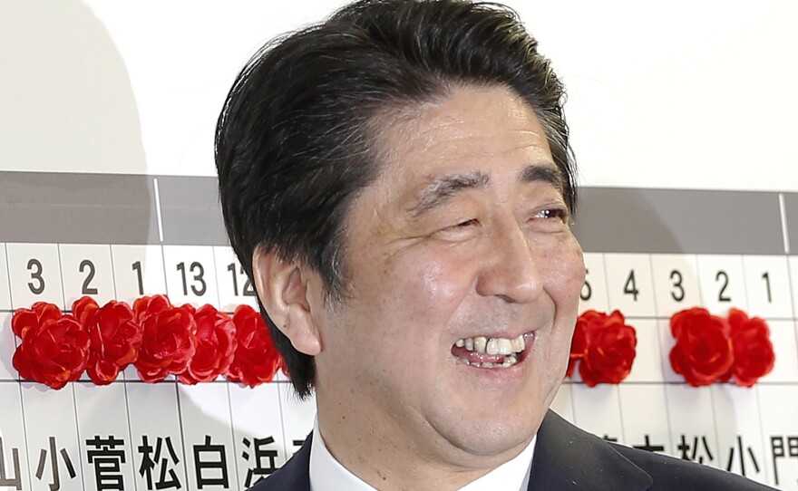 Japanese Prime Minister Shinzo Abe, leader of the Liberal Democratic Party, smiles as he places a red rosette on the name of his Liberal Democratic Party's winning candidate during ballot counting.
