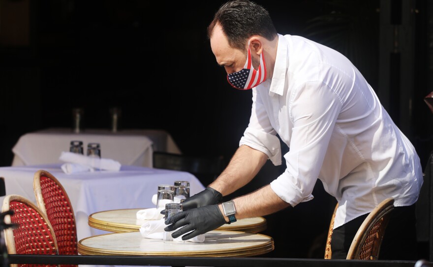 A restaurant server in New York prepares a table. But people remain cautious about going out and spending money.