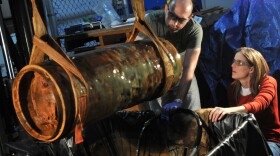 Paul Mardikian and Claudia Chemello, conservationists from Terra Mare Conservation, document the state of a Howell Torpedo at a Naval History and Heritage Command (NHHC) warehouse. 